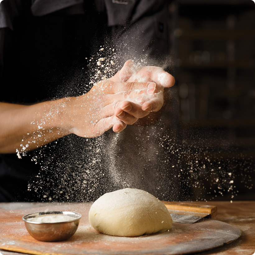 Hands tossing flour over pizza dough